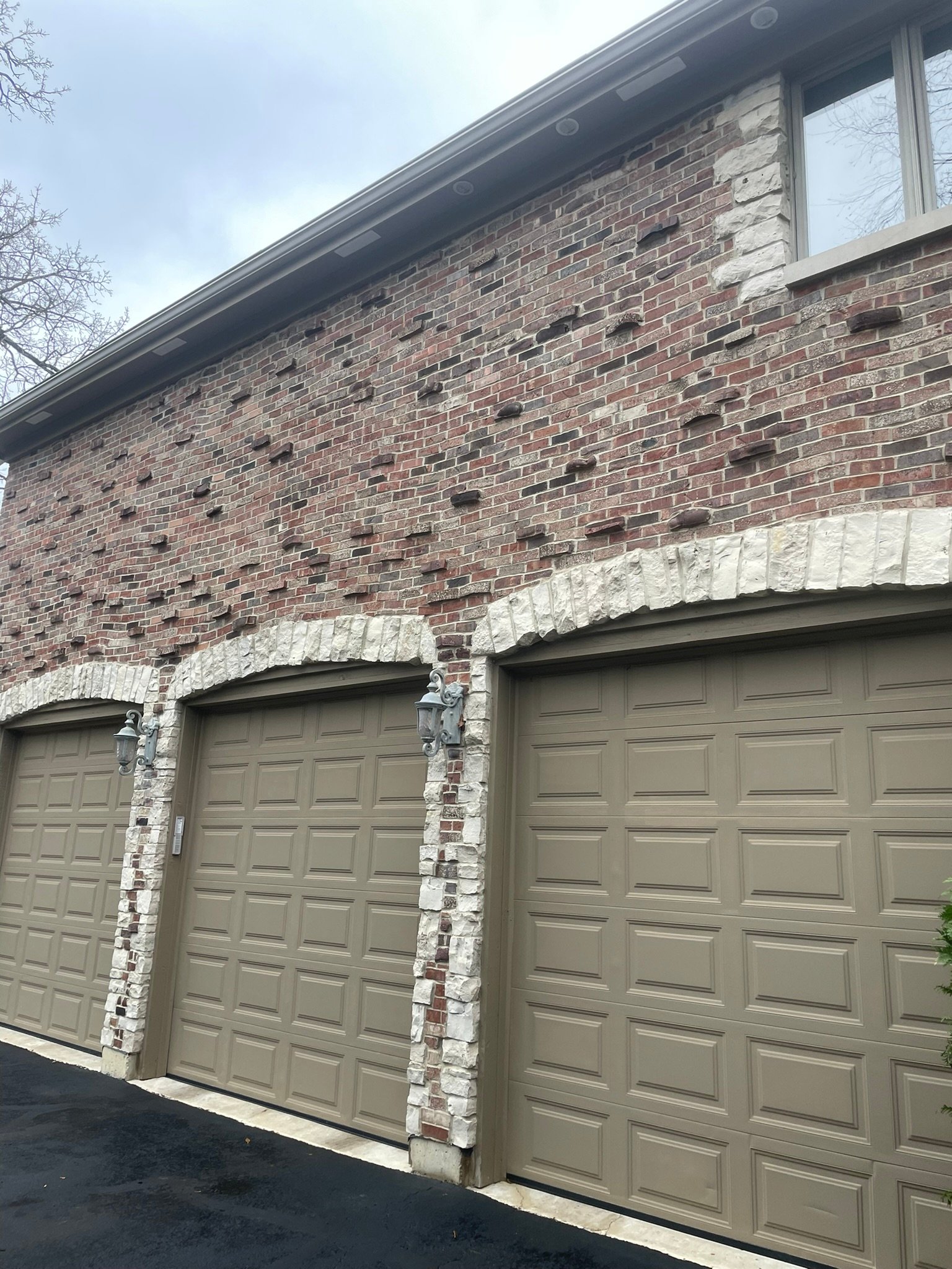 Brick and stone garage facade with three new tan garage doors after exterior updates